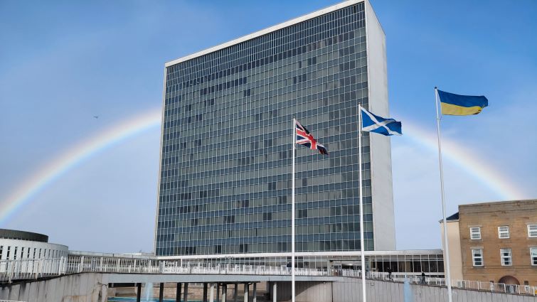 This is an image of South Lanarkshire Council HQ, with flags of the UK, Scotland and Ukraine in the foreground and a rainbow dissecting the building in the background