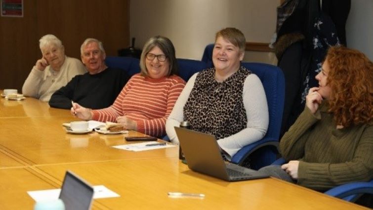 This image shows a number of people sitting round a desk