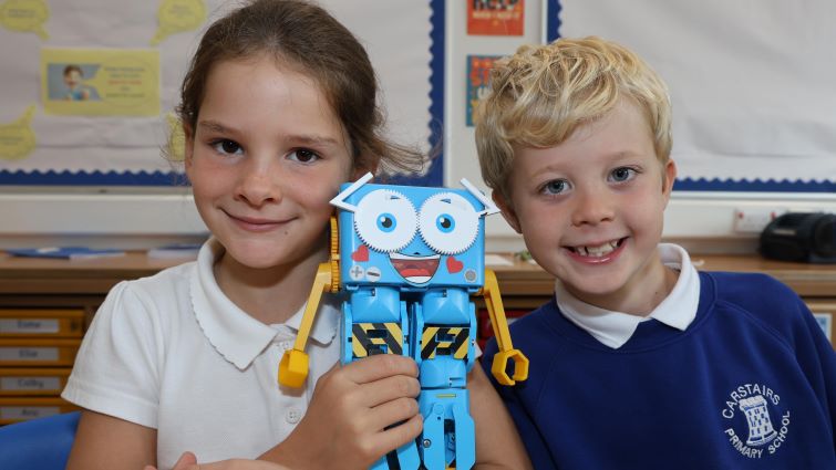 A boy and girl are pictured in teh classroom with the robot assistant that helped the school win a digital coding prize recently.