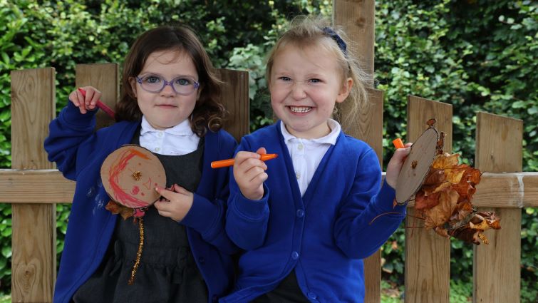 Two junior girls smile as they show off their outdoor artwork.