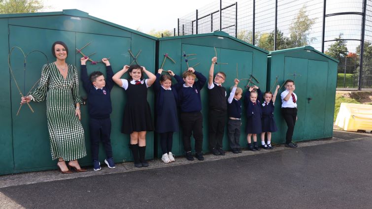 The Head Teacher and a group of children are lined up in the playground holding twig letters spelling the word excellent.